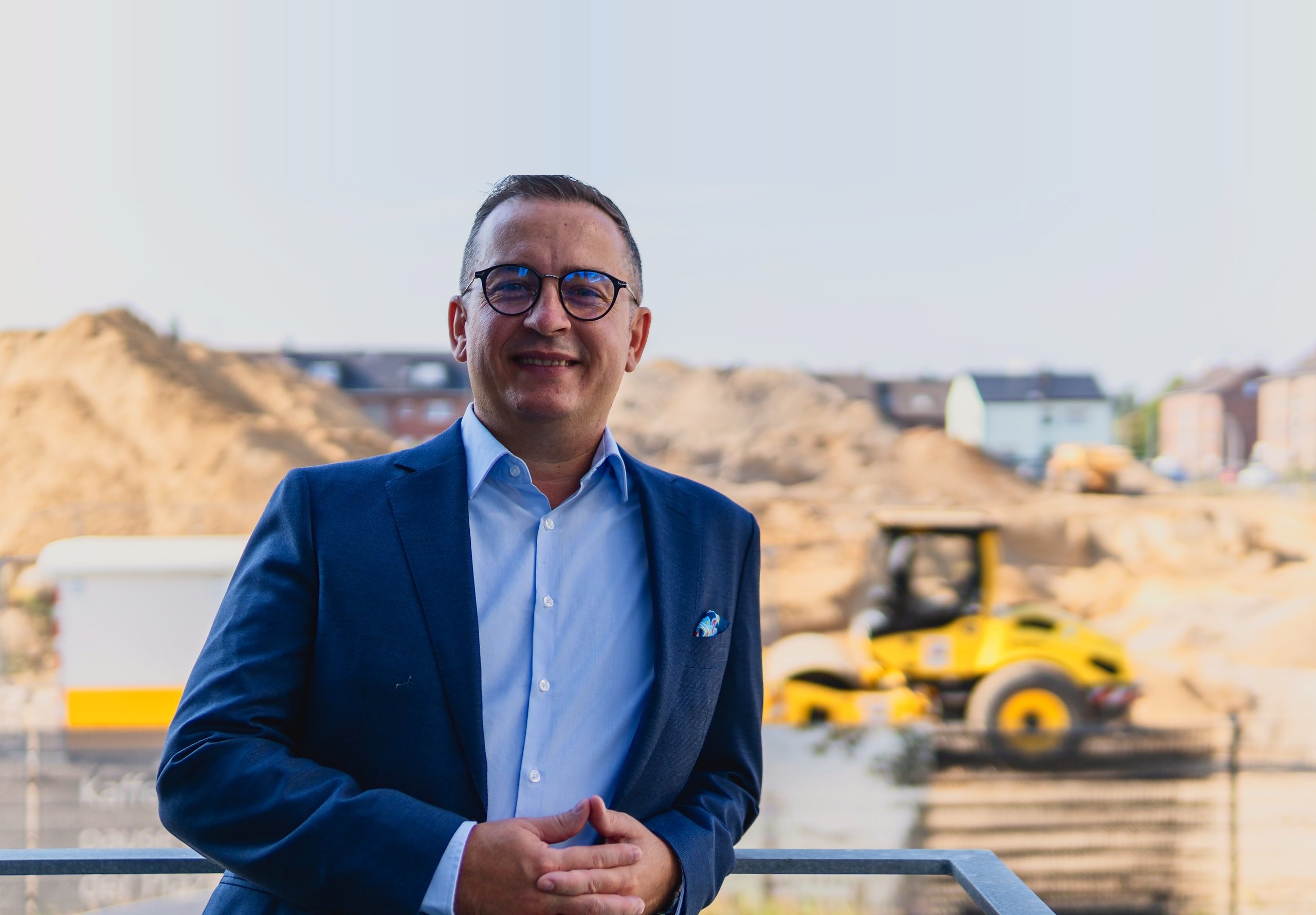 Alexander Motyl auf der Baustelle eines Neubauprojekts, im Hintergrund Erdaushub und eine Walze.