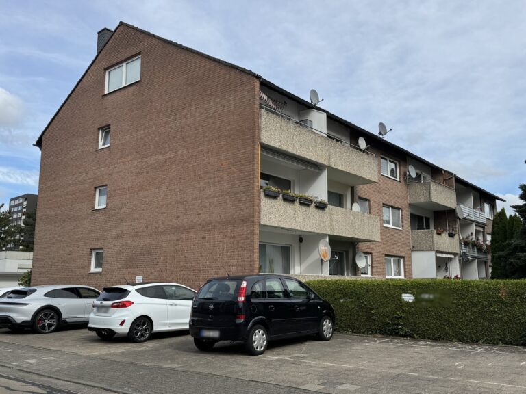 Mehrfamilienhaus mit Klinkergiebel und Balkonen, Stellplätze vor dem Haus