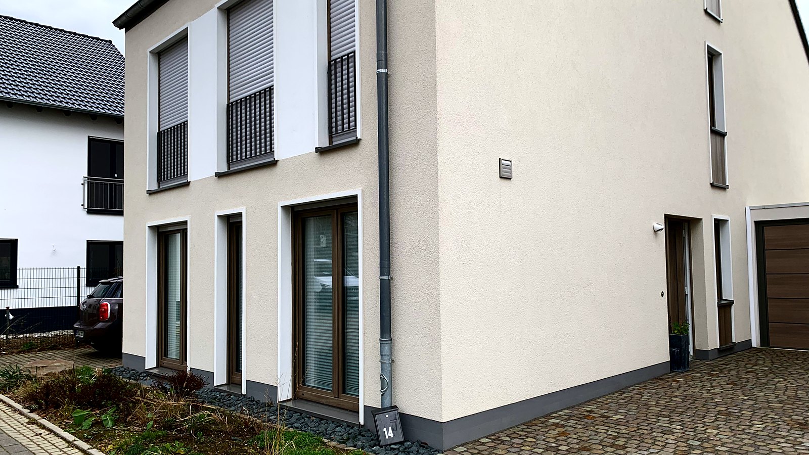 Straßenansicht eines fertiggestellten Hauses der Zündorfer Stadtgärten mit Putzfassade, Garage und gepflasterter Zufahrt.
